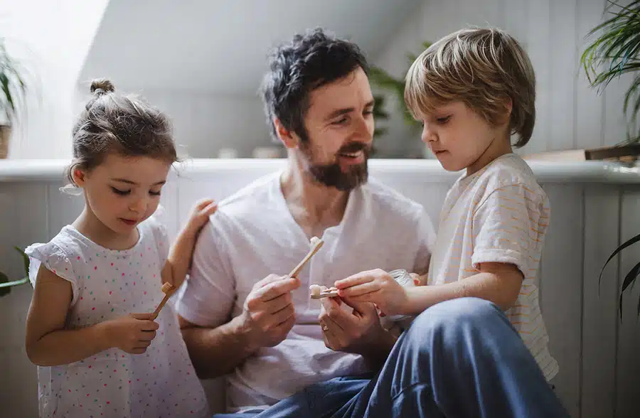 Father With Two Small Children Brushing Teeth Indoors At Home