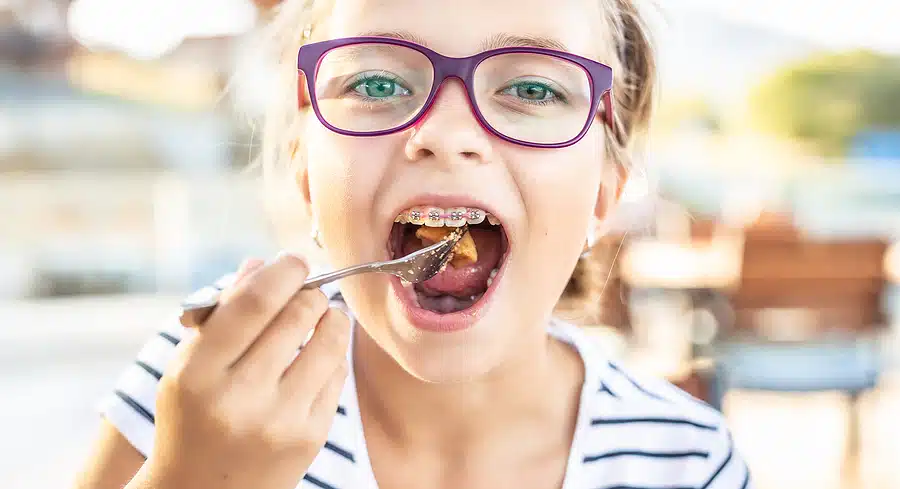 Young Girl Wearing Glasses And Braces Puts Food On Fork Into Her